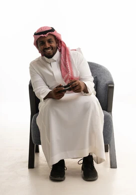 Interaction and immersion with video games, spending enjoyable and entertaining time, using modern electronic entertainment devices and technologies, a portrait of a Saudi Arabian Gulf man wearing traditional attire and a headscarf holding a game controller, with a white background.