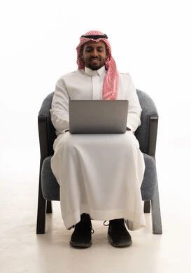 استخدام التقنيات الحديثة ، إجراء مكالمات الفيديو مع الأهل والأصدقاء، اجتماع عمل عن بعد، بورتريه لرجل عربي خليجي سعودي يرتدي الثوب التقليدي والشماغ يمسك جهاز الحاسوب المحمول وينظر إليه بإيماءات السعادة، خلفية بيضاء