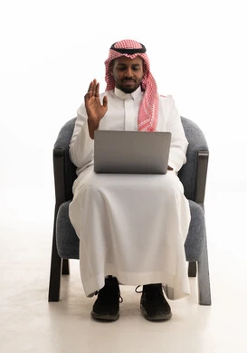 Making video calls with family and friends, a remote work meeting, a portrait of a Saudi Arabian Gulf man wearing traditional attire and a ghutrah, holding a laptop and looking at it with gestures of happiness, white background.