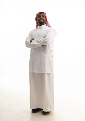 الوقوف بايدي متقاطعة ،العمل في القطاع الصحي السعودي، إجراء الفحوصات اللازمة، مفهوم الطب والرعاية الصحية ، بورتريه لطبيبب سعودي خليجي مبتسم يرتدي الشماغ والزي التقليدي والمعطف الابيض  يقدم خدماته للمرضى بكل كفاءه،  خلفية بيضاء