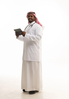 دمج التكنولوجيا  الحديثة بالعمل ، مفهوم الطب والرعاية الصحية ، بورتريه لطبيبب سعودي خليجي مبتسم يرتدي الشماغ والزي التقليدي والمعطف الابيض ينظر للكاميرا يقدم خدماته للمرضى بكل كفاءه ويستخدم الجهاز اللوحي،  خلفية بيضاء