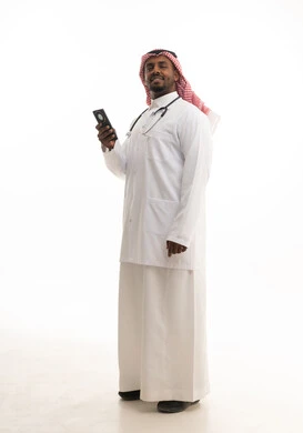 بورتريه لطبيبب سعودي خليجي مبتسم يرتدي الشماغ والزي التقليدي والمعطف الابيض ينظر للكاميرا يقدم خدماته للمرضى بكل كفاءه ويستخدم الهاتف المحمول، استخدام التقنيات الحديثة فى العمل ، مفهوم الطب والرعاية الصحية ،  خلفية بيضاء