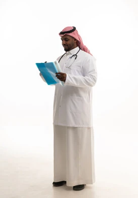 مفهوم الطب والرعاية الصحية ، بورتريه لطبيبب سعودي خليجي مبتسم يرتدي الشماغ والزي التقليدي والمعطف الابيض ينظر للكاميرا يقدم خدماته للمرضى بكل كفاءه، كتابة التقارير الطبية ، تدوين الملاحظات اللازمة ،  خلفية بيضاء