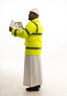 مفهوم الهندسة والانشاءات المعمارية، بورتريه من الجانب لمهندس عربي خليجي سعودي يرتدي الثوب التقليدي والسترة الخاصة وخوذة الحماية يقف وبيده مخطط هندسي ،المتابعة والإشراف على العمل بشكل مباشر، الإعمار بسواعد أبناء الوطن، الجسم بالطول الكامل، خلفية بيضاء