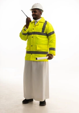Monitoring and supervising work using a technical device, construction by the hands of the nation's sons, the concept of engineering and architectural constructions, a portrait of a Saudi Gulf Arab engineer wearing traditional attire and a special jacket and safety helmet, standing with an engineering plan in hand, full-body, white background.