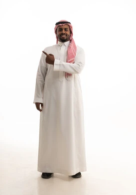 حركات تدل على هذا المكان (هنا), الدلالة على موقع معين,تحديد مكان عنصر محدد, بورتريه لرجل عربي خليجي سعودي مبتسم يرتدي الشماغ والثوب التقليدي يشير بإصبع السبابة إلى شيء ما, الجسم بالطول الكامل, خلفية بيضاء
