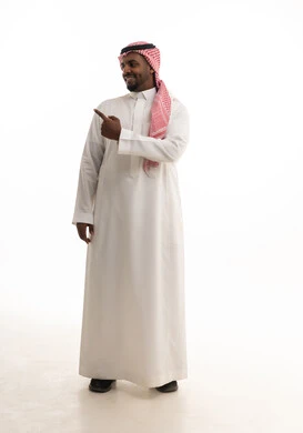 الدلالة على موقع معين, حركات تدل على هذا المكان (هنا), تحديد مكان عنصر محدد, بورتريه لرجل عربي خليجي سعودي مبتسم يرتدي الشماغ والثوب التقليدي يشير بإصبع السبابة إلى شيء ما, الجسم بالطول الكامل, خلفية بيضاء