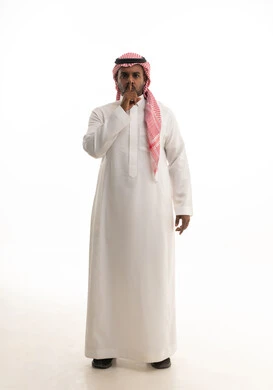 Silence and stillness and no disturbance, a portrait of an Arab Gulf Saudi man wearing traditional attire and a shemagh, placing his index finger on his mouth, stopping talking and lowering the voice, requesting silence and quiet, finger movement and gestures, white background.