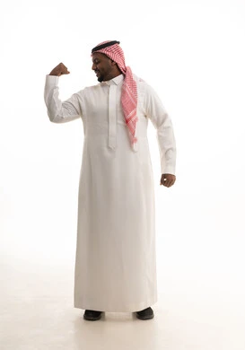 لياقة بدنية وصحة، إستعراض القوة البدنية ،بورتريه لرجل عربي خليجي سعودي مبتسم يرتدي الشماغ والثوب التقليدي يرفع يده بكفه مقبوضه ، مفهوم القوة العضلية وعرض العضلات ، خلفية بيضاء
