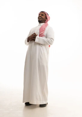 تعابير البهجة والسرور الشديد, الشعور بالفرح والسعادة، بورتريه لرجل عربي خليجي سعودي يرتدي الثوب التقليدي والشماغ يضع يده على بطنه بإيماءات الضحك وينظر إلى الكاميرا، الطول الكامل للجسم، خلفية بيضاء