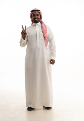 Raising the sign of victory and peace, a symbol of winning and triumph, achieving goals and ambitions, completing assigned tasks, signals and movements of body language, a portrait of an Arab Gulf Saudi man wearing traditional attire and a shemagh looking at the camera with gestures of happiness and joy, full-body, white background.
