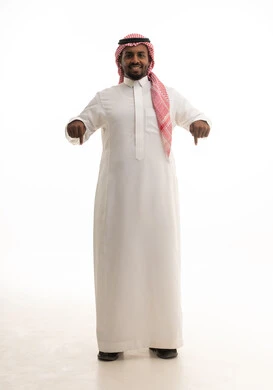 Indication of a specific location, gestures that indicate this place (here), identifying the location of a specific element, a portrait of a smiling Saudi Arabian Gulf man wearing a ghutrah and traditional thobe pointing with his index finger to something, full-body, white background.