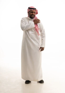 The feeling of severe, unbearable pain in the shoulder, difficulty in movement and bending the arm, a portrait of an Arab Gulf Saudi man wearing traditional attire and a ghutrah, suffering from joint pain, facial expressions indicating distress, white background.