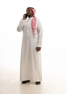 إجراء مكالمة هاتفية مع الأهل والأصدقاء، تصفح مواقع التواصل الاجتماعي ، دمج التقنيات الحديثة فى الحياة اليومية ، استخدام الهاتف المحمول ، بورتريه لرجل عربي خليجي سعودي يرتدي الثوب التقليدي والشماغ يمسك الجوال بيده ، خلفية بيضاء