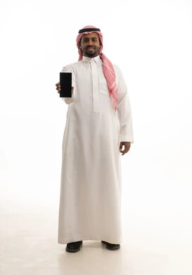 عرض شاشة سوداء فارغة ، تصفح مواقع التواصل الاجتماعي ، دمج التقنيات الحديثة فى الحياة اليومية ، استخدام الهاتف المحمول ،بورتريه لرجل عربي خليجي سعودي يرتدي الثوب التقليدي والشماغ يمسك الجوال بيده ، خلفية بيضاء