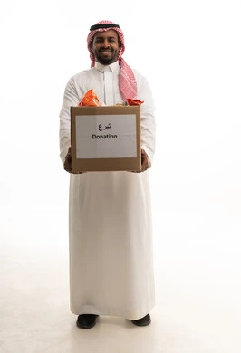 A volunteer event and charitable work, a humanitarian initiative and donation, a portrait of a Saudi Arabian Gulf man wearing a ghutrah and traditional thobe holding a cleaning supplies box, looking at the camera with gestures of joy, donating to the mosque cleaning project at the Islamic Association in the Kingdom, white background.