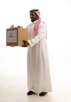A volunteer event and charitable work, a humanitarian initiative and donation, a portrait of a Saudi Arabian Gulf man wearing a ghutrah and traditional thobe holding a cleaning supplies box, looking at the camera with gestures of joy, donating to the mosque cleaning project at the Islamic Association in the Kingdom, white background.