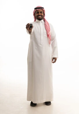 تعابير الفرح لامتلاك سيارة جديدة, النظر إلى الكاميرا بإيماءات السعادة و السرور, بورتريه لرجل عربي خليجي سعودي مبتسم يرتدي الثوب التقليدي و الشماغ يمسك بيده مفتاح التحكم عن بعد, صورة للجسم بالطول الكامل, خلفية بيضاء