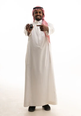 Looking at the camera with gestures of happiness and joy, expressions of delight at owning a new car, a portrait of a smiling Saudi Arabian Gulf man wearing traditional attire and a ghutrah, pointing with his index finger to the remote control key, a full-body image, white background.