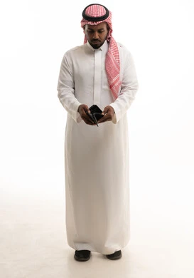 Expressions of sadness and depression, the concept of bankruptcy and lack of money, a portrait of a Saudi Arabian Gulf man wearing traditional attire and a ghutrah, opening an empty leather wallet in his hand, gestures of poverty and the need for money and assistance, white background.