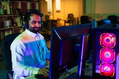 ايماءات الاندماج و التركيز، مفهوم الإبداع في عالم المونتاج وصناعة المحتوى المرئي، صورة من الجانب لمونتير عربي خليجي سعودي يرتدي الثوب الابيض و سماعات الراس يجلس أمام شاشة حاسب محمول يقوم باخراج مشهد سينمائي