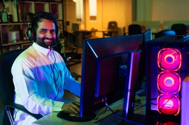 مفهوم الإبداع في عالم المونتاج وصناعة المحتوى المرئي، صورة من الجانب لمونتير عربي خليجي سعودي يرتدي الثوب الابيض و سماعات الراس يجلس أمام شاشة حاسب محمول يقوم باخراج مشهد سينمائي ، ايماءات الاندماج و التركيز