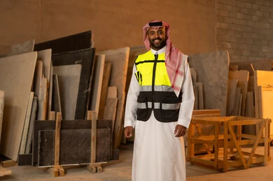 Quality of local national production, home and office furniture industry, a Saudi Arabian Gulf Arab engineer man wearing traditional thobe and work clothes looking at the camera with happy gestures, standing straight with expressions of pleasure, workshops in the Kingdom of Saudi Arabia, tools and equipment made of marble