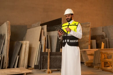 Using technology in laboratories, workshops in Saudi Arabia, tools and equipment made of marble, quality of local national production, home and office furniture manufacturing, a Saudi Arabian Gulf Arab engineer wearing traditional thobe and work clothes holding a tablet in his hand