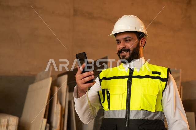 العمل على الهاتف المحمول، ورشات عمل في المملكة العربية السعودية, أدوات ومعدات مصنوعة من الرخام، جودة الانتاج المحلي الوطني, صناعة الأثاث المنزلي والمكتبي، رجل مهندس عربي خليجي سعودي يرتدي الثوب التقليدي وزي العمل يمسك بيده الجوال