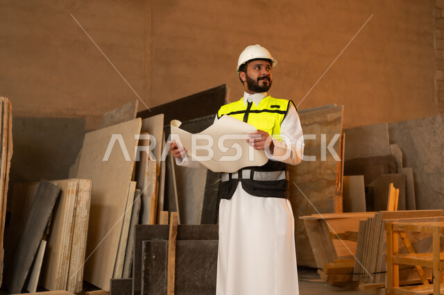 العمل على المخططات والاوراق الهندسية، رجل مهندس عربي خليجي سعودي يرتدي الثوب التقليدي وزي العمل يمسك بيده الورقة، ورشات عمل في السعودية، أدوات ومعدات مصنوعة من الرخام، جودة الانتاج المحلي الوطني, صناعة الأثاث المنزلي والمكتبي
