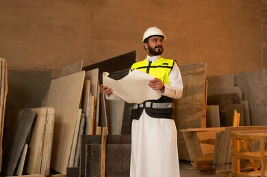 Working on engineering plans and papers, a Saudi Arabian Gulf Arab engineer wearing traditional thobe and work clothes holding a paper in his hand, workshops in Saudi Arabia, tools and equipment made of marble, quality of local national production, home and office furniture manufacturing