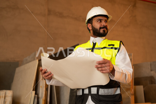 العمل على المخططات والاوراق الهندسية، رجل مهندس عربي خليجي سعودي يرتدي الثوب التقليدي وزي العمل يمسك بيده الورقة، ورشات عمل في السعودية، أدوات ومعدات مصنوعة من الرخام، جودة الانتاج المحلي الوطني, صناعة الأثاث المنزلي والمكتبي