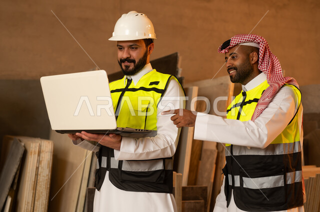 رجلان مهندسان عربيان خليجيان سعوديان يرتديان الثوب التقليدي وزي العمل يعملان على الحاسب المحمول، دمج التقنية والتكنولوجيا في المعامل، ورشات عمل في السعودية، أدوات ومعدات مصنوعة من الرخام، جودة الانتاج المحلي الوطني, صناعة الأثاث المنزلي والمكتبي
