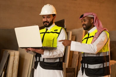 رجلان مهندسان عربيان خليجيان سعوديان يرتديان الثوب التقليدي وزي العمل يعملان على الحاسب المحمول، دمج التقنية والتكنولوجيا في المعامل، ورشات عمل في السعودية، أدوات ومعدات مصنوعة من الرخام، جودة الانتاج المحلي الوطني, صناعة الأثاث المنزلي والمكتبي