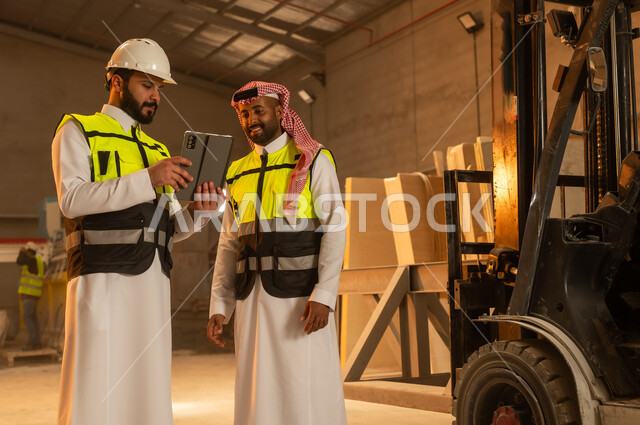 ورشات عمل في المملكة العربية السعودية, أدوات ومعدات مصنوعة من الرخام، جودة الانتاج المحلي الوطني, صناعة الأثاث المنزلي والمكتبي، رجلان مهندسان عربيان خليجيان سعوديان يرتديان الثوب التقليدي وزي العمل يعملان على جهاز التابلت، دمج التقنية والتكنولوجيا في المعامل
