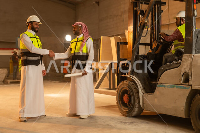Greetings, greetings, and handshakes. Workshops in Saudi Arabia. Marble tools and equipment. Quality local national production. Traditional folk professions and crafts in the Kingdom. Home and office furniture manufacturing. A Saudi Arabian Gulf engineer wearing traditional clothing and work clothes shakes hands with his colleague.