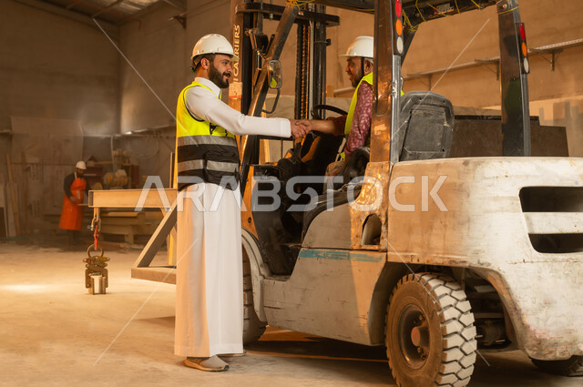 السلام والترحيب والمصافحة، ورشات عمل في السعودية, أدوات ومعدات مصنوعة من الرخام, جودة الانتاج المحلي الوطني, مهن وحرف شعبية تقليدية قديمة في المملكة, صناعة الأثاث المنزلي والمكتبي، رجل مهندس عربي خليجي سعودي يرتدي الثوب التقليدي وزي العمل يصافح زميله