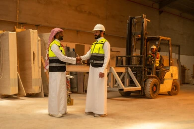 Peace, welcome and handshake, workshops in Saudi Arabia, tools and equipment made of marble, quality of local national production, old traditional professions and crafts in the Kingdom, home and office furniture manufacturing, a Saudi Arabian Gulf Arab engineer wearing traditional thobe and work clothes shaking hands with his colleague