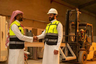 Greetings, greetings, and handshakes. Workshops in Saudi Arabia. Marble tools and equipment. Quality local national production. Traditional folk professions and crafts in the Kingdom. Home and office furniture manufacturing. A Saudi Arabian Gulf engineer wearing traditional clothing and work clothes shakes hands with his colleague.