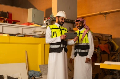 ورشات عمل في المملكة العربية السعودية, أدوات ومعدات مصنوعة من الرخام، جودة الانتاج المحلي الوطني, صناعة الأثاث المنزلي والمكتبي، رجلان مهندسان عربيان خليجيان سعوديان يرتديان الثوب التقليدي وزي العمل يعملان على جهاز التابلت، دمج التقنية والتكنولوجيا في المعامل