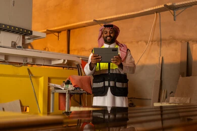 Integrating technology and technology in laboratories, workshops in Saudi Arabia, tools and equipment made of marble, quality of local national production, home and office furniture manufacturing, a Saudi Arabian Gulf Arab engineer man wearing traditional thobe and work clothes holding a tablet in his hand