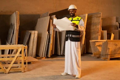 العمل على المخططات والاوراق الهندسية، رجل مهندس عربي خليجي عماني يرتدي الدشداشة وزي العمل يمسك بيده الورقة، ورشات عمل في سلطنة عمان، أدوات ومعدات مصنوعة من الرخام، جودة الانتاج المحلي الوطني, صناعة الأثاث المنزلي والمكتبي