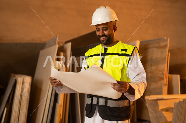 العمل على المخططات والاوراق الهندسية، رجل مهندس عربي خليجي عماني يرتدي الدشداشة وزي العمل يمسك بيده الورقة، ورشات عمل في سلطنة عمان، أدوات ومعدات مصنوعة من الرخام، جودة الانتاج المحلي الوطني, صناعة الأثاث المنزلي والمكتبي