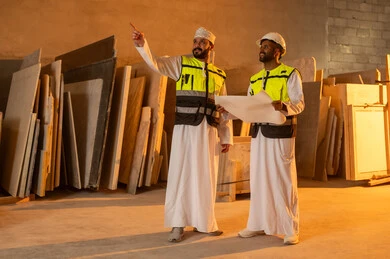 Exchanging opinions and experiences, workshops in the Sultanate of Oman, tools and equipment made of marble, quality of local national production, home and office furniture manufacturing, an Arab Gulf Omani engineer man wearing a dishdasha and work clothes discussing with his colleague