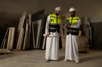 Home and office furniture manufacturing, two Omani Gulf Arab engineers wearing dishdashas and work clothes working on a tablet, integrating technology into laboratories, factories and workshops in the Sultanate of Oman, tools and equipment made of marble, quality of local national production