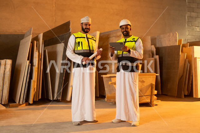 Quality of local national production, home and office furniture industry, two Omani Gulf Arab engineers wearing dishdashas and work clothes working on a tablet, integrating technology and technology in laboratories, factories and workshops of the Sultanate of Oman, tools and equipment made of marble