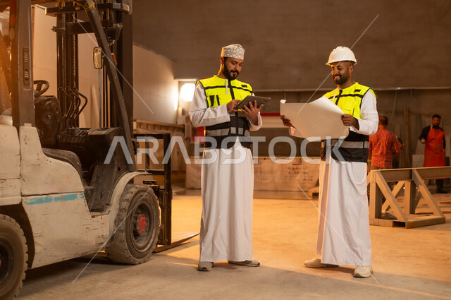 Factories and plants of the Sultanate of Oman, tools and equipment made of marble, quality of local national production, home and office furniture industry, two Omani Gulf Arab engineers wearing dishdashas and work clothes working on a tablet, integrating technology and technology in laboratories