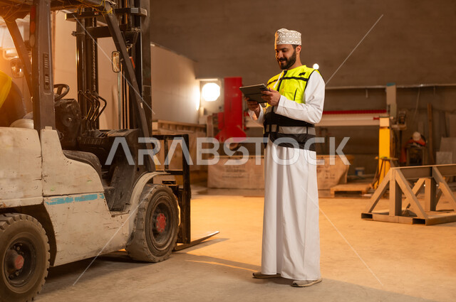 Integrating technology and technology in laboratories, workshops in the Sultanate of Oman, tools and equipment made of marble, quality of local national production, home and office furniture manufacturing, an Arab Gulf Omani engineer man wearing a dishdasha and work clothes holding a tablet in his hand