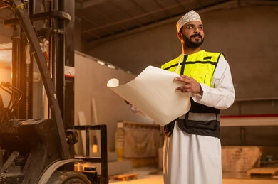 Making a local national product, making home and office furniture, working on engineering plans and papers, an Arab Gulf Omani engineer wearing a dishdasha and work clothes holding a paper in his hand, workshops in the Sultanate of Oman, tools and equipment made of marble