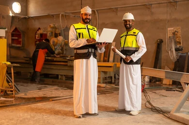 صناعة الأثاث المنزلي والمكتبي، رجلان مهندسان عربيان خليجيان عمانيان يرتديان الدشداشة وزي العمل يعملان على الحاسب المحمول، دمج التقنية والتكنولوجيا في المعامل، ورشات عمل في سلطنة عمان، أدوات ومعدات مصنوعة من الرخام، جودة الانتاج المحلي الوطني